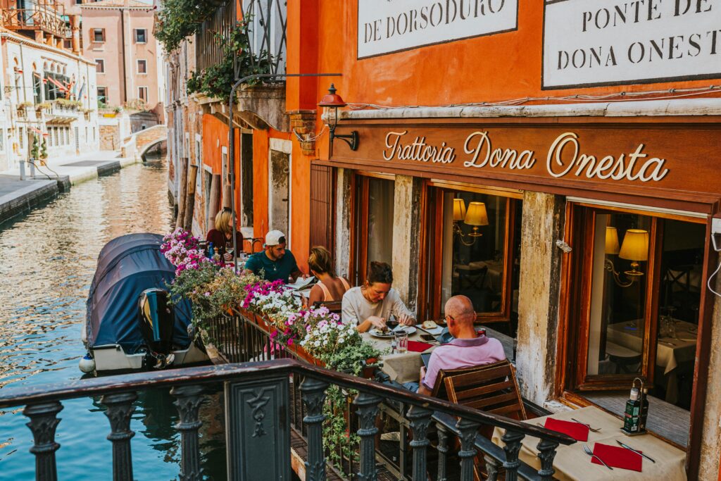 pexels photo 15710118 15710118 Cozy Venetian canal-side restaurant with patrons enjoying a meal. Ideal travel destination.